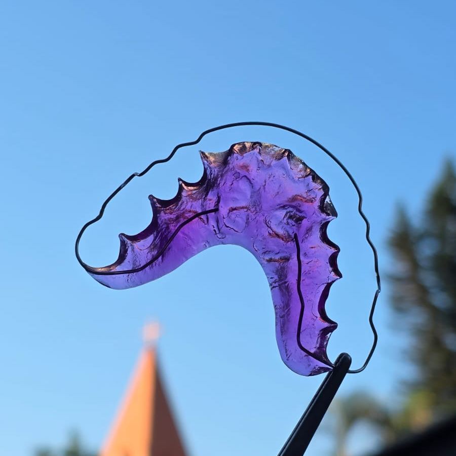 Aparelho de contenção móvel em acrílico roxo com fio metálico, segurado por pinça contra o céu